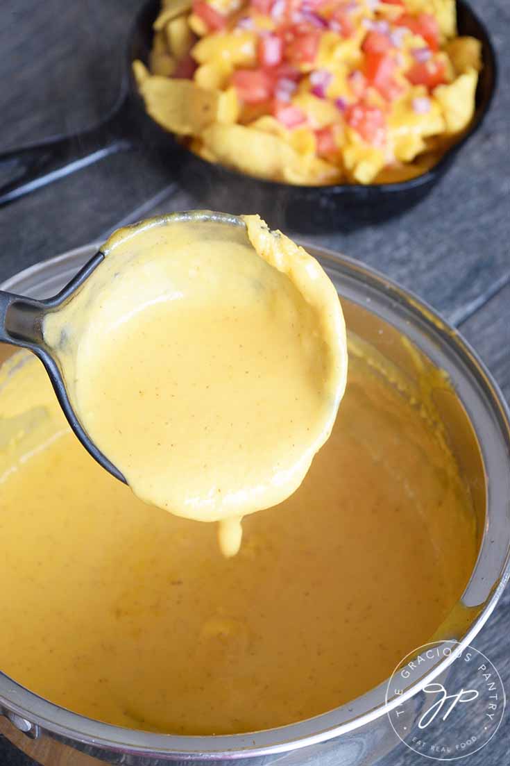 Delicious Nacho Cheese Sauce being ladled out of the pot and onto some corn chips.