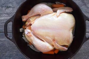 A whole chicken sitting on top of the veggies in the dutch oven.