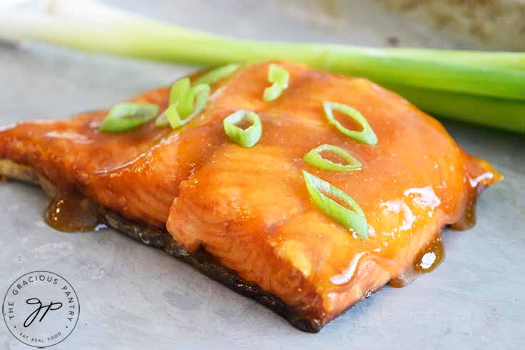 A horizontal shot of a Teriyaki Salmon fillet, just cooked, and glazed with sauce and fresh green onions.