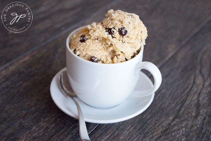 Horizontal shot of the finished edible cookie dough recipe served in a white mug on a white saucer.