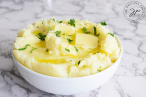 A horizontal shot of Instant Pot mashed potatoes in a white bowl with melted butter and chopped, fresh herbs.