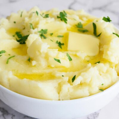 Instant Pot mashed potatoes in a white bowl with a pat of butter melting and fresh herbs sprinkled over the top.