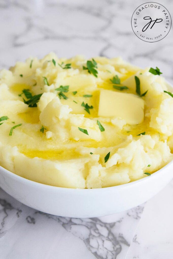 Instant Pot mashed potatoes in a white bowl with a pat of butter melting and fresh herbs sprinkled over the top.
