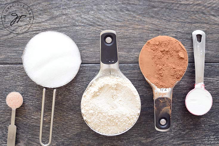 Mug cake mix ingredients lined up in their measuring cups and spoons.