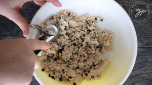Scooping the cookie dough out of the bowl with an ice cream scoop.
