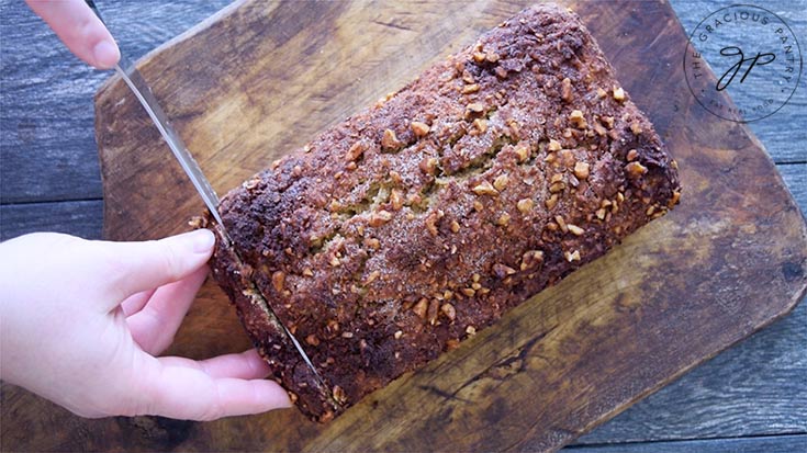 Slicing the loaf of apple bread on a cutting board.