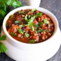 A white crock filled with turkey chili, garnished with fresh herbs.