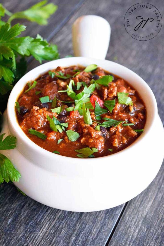 A white crock filled with turkey chili, garnished with fresh herbs.