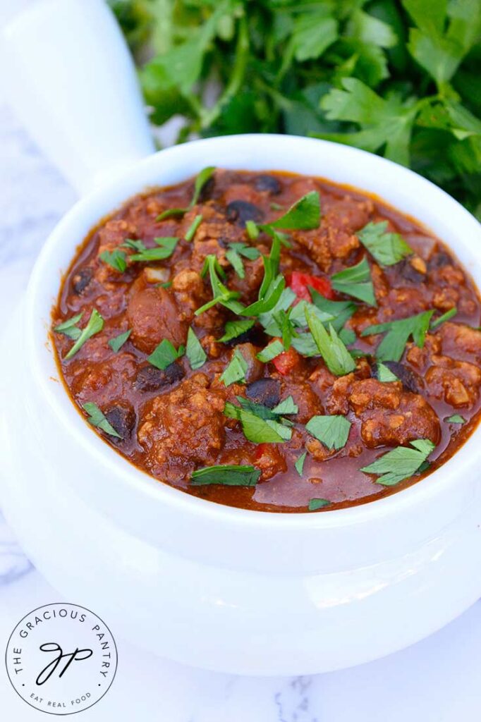 A side view of a crock of turkey chili. Fresh herbs lay behind the bowl.