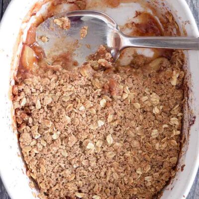 A casserole dish with apple crisp that has been partially scooped out.