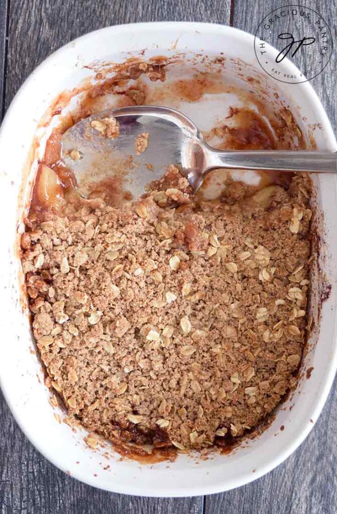 A casserole dish with apple crisp that has been partially scooped out.