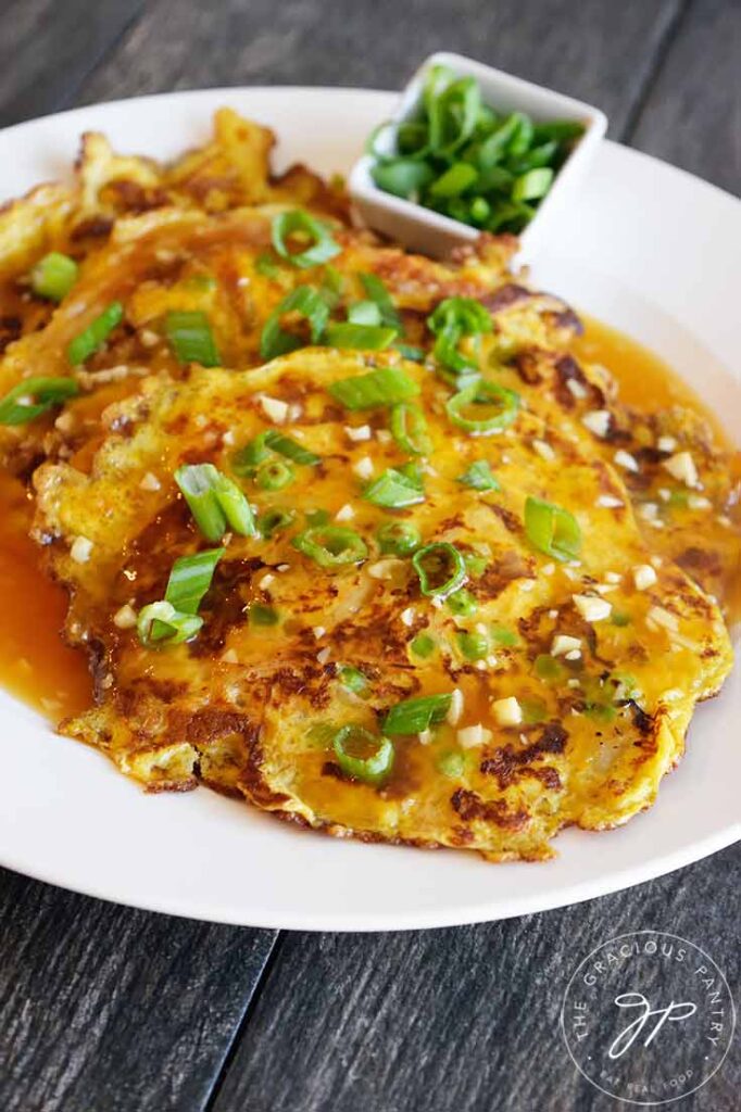 A closer view of a white platter of Egg Foo Young topped with gravy and green onions.