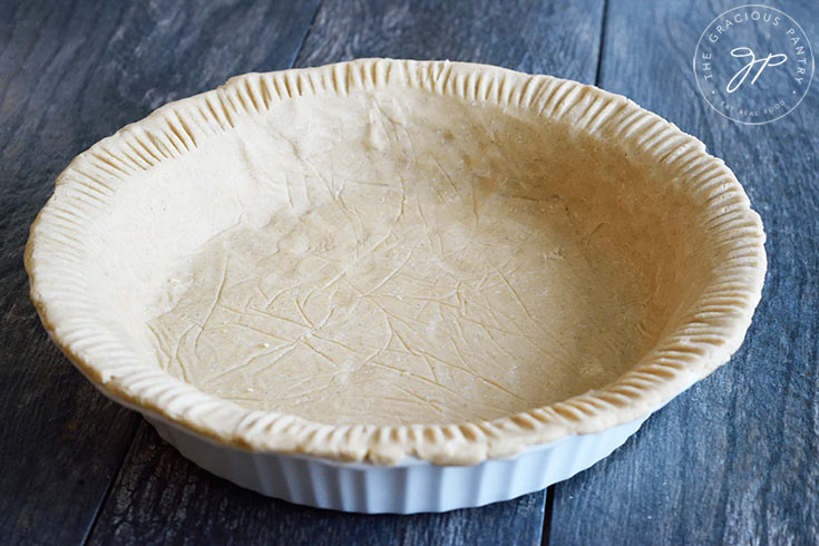 A horizontal shot of the finished Oat Flour Pie Crust in a white pie pan on a dark gray background.