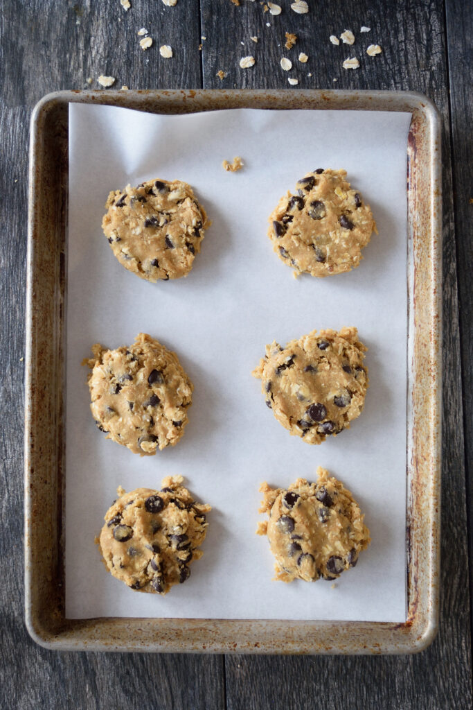 Flattened, raw, oatmeal chocolate chip cookies on a cookie sheet, waiting to go into the oven for baking.