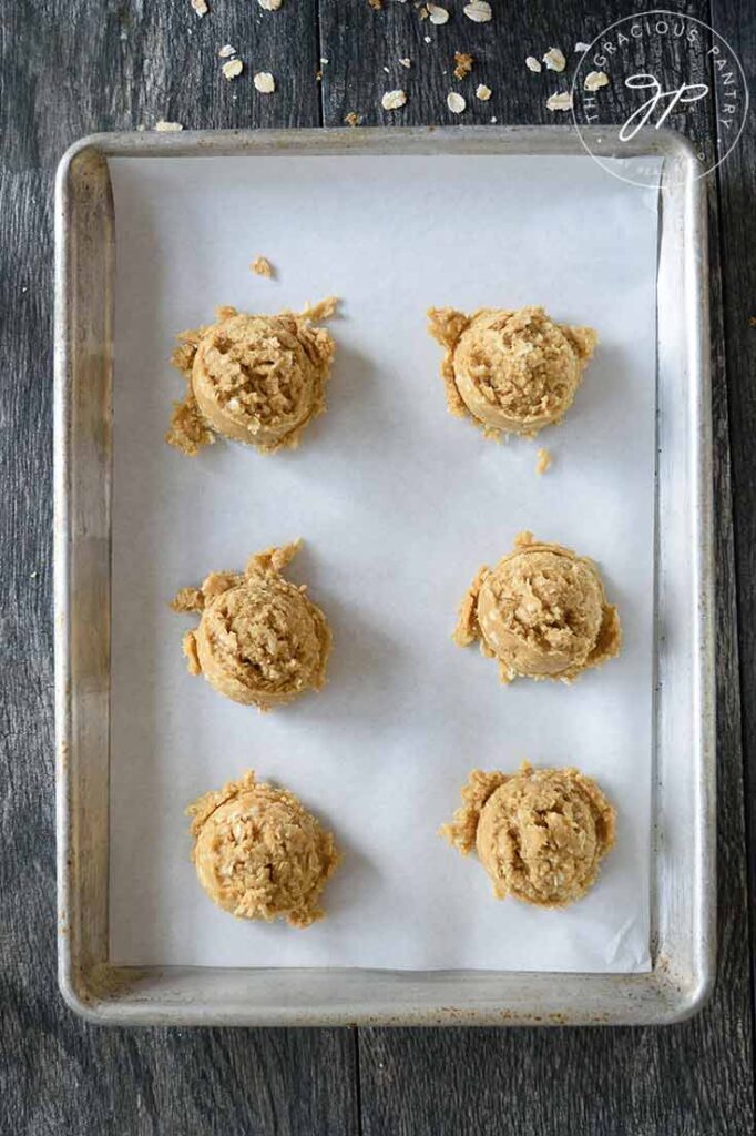 Scooped oatmeal cookie dough sitting on a parchment lined cookie sheet waiting to be put into the oven.