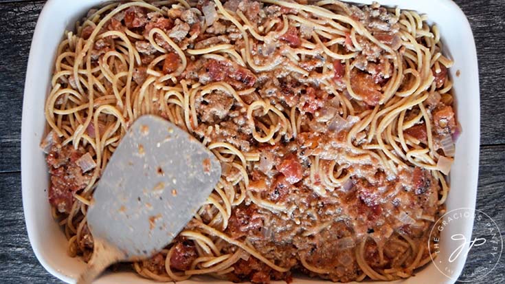 Flattening out the pasta in the casserole dish with the back of the spatula.