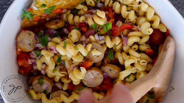 Mixing the cavatappi pasta to coat in dressing.