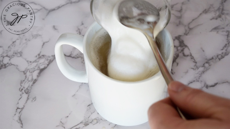 Pouring the frothed milk into the mug of tea to make a London fog.