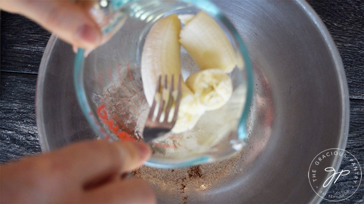 Mashing the banana with a fork before adding it to the mixing bowl.