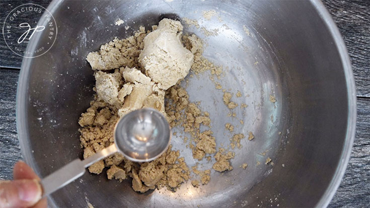 Adding one tablespoon of water to the still crumbly pie crust dough.