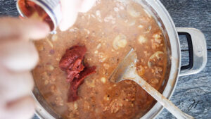 Adding tomato paste to the lasagna soup.