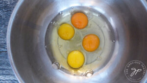 4 cracked eggs sitting in a large mixing bowl.