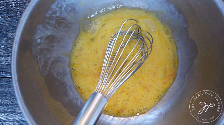 The eggs sit whisked in the mixing bowl with the whisk still sitting in the bowl.