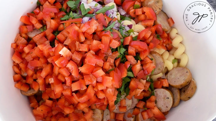 Chopped red bell peppers added to the bowl of pasta.