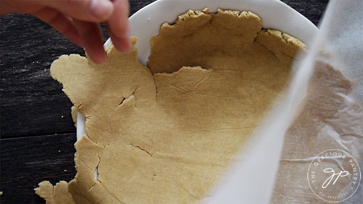 Turning the rolled pie crust over into a white pie pan.