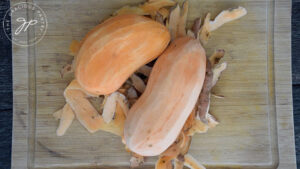 Two sweet potatoes lay on a bed of their peels.