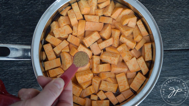 A pot with chopped sweet potatoes, chicken broth and nutmeg being added.