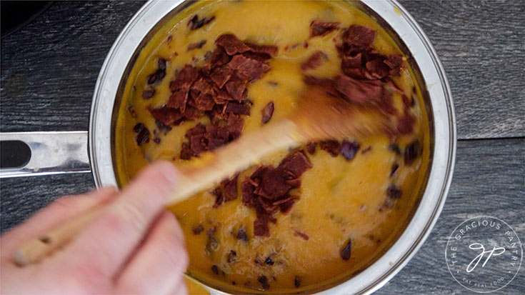 Stirring cooked bacon into the pot of Bacon Sweet Potato Soup.