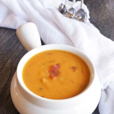 A bowl of this Bacon Sweet Potato Soup sits on a table with a white towel to the side and some measuring spoons in the background.