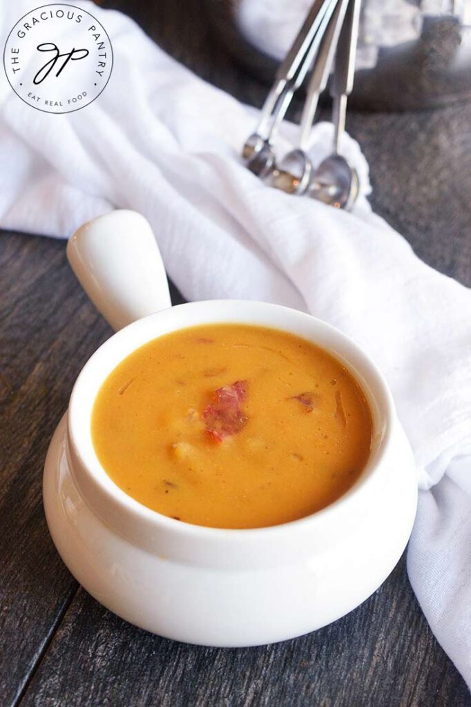 A bowl of this Bacon Sweet Potato Soup sits on a table with a white towel to the side and some measuring spoons in the background.