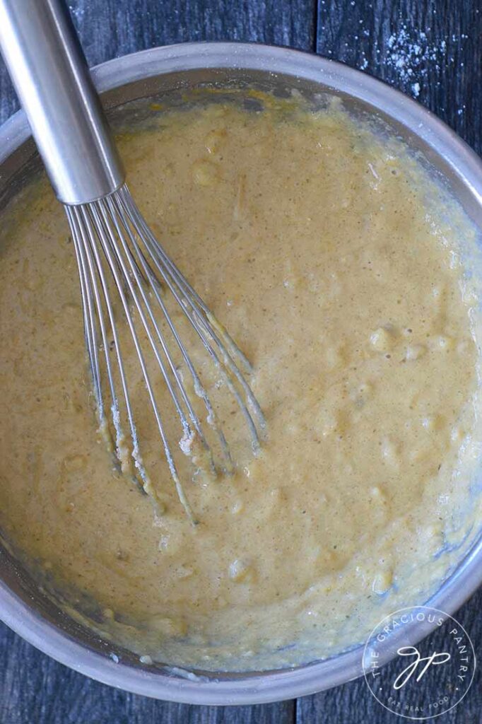 Oat Flour Banana Bread batter in a mixing bowl with a whisk resting in the batter.