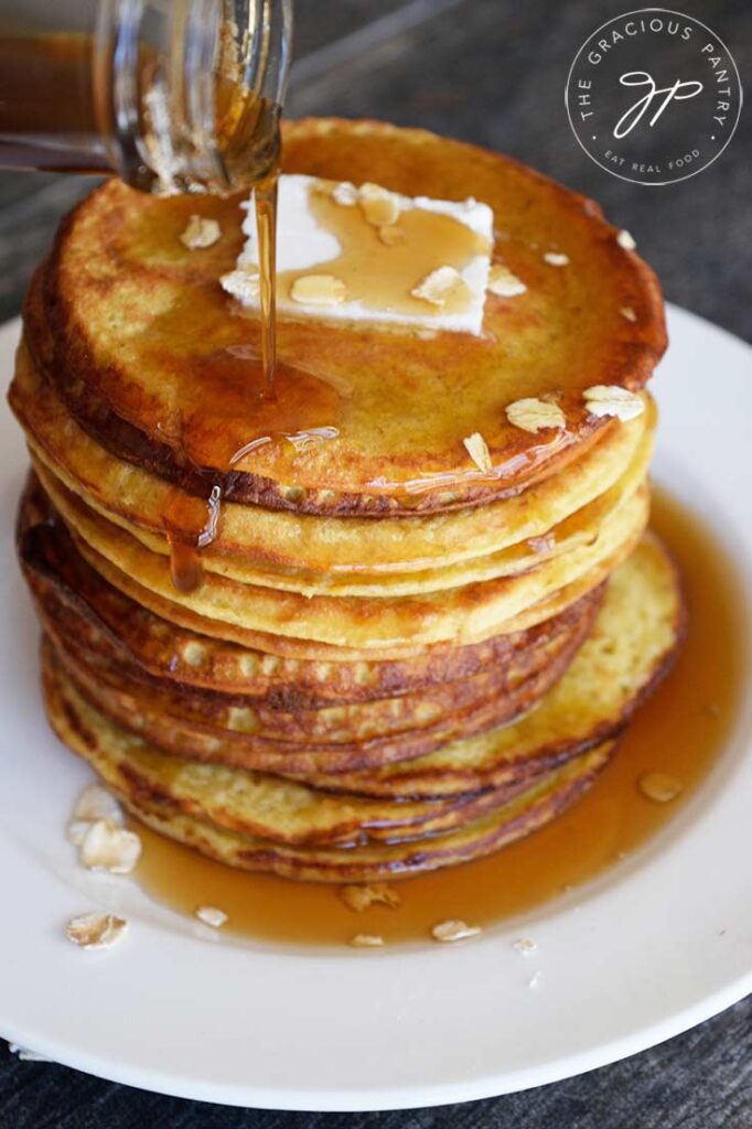 A stack of oat pancakes with maple syrup being poured over the top.