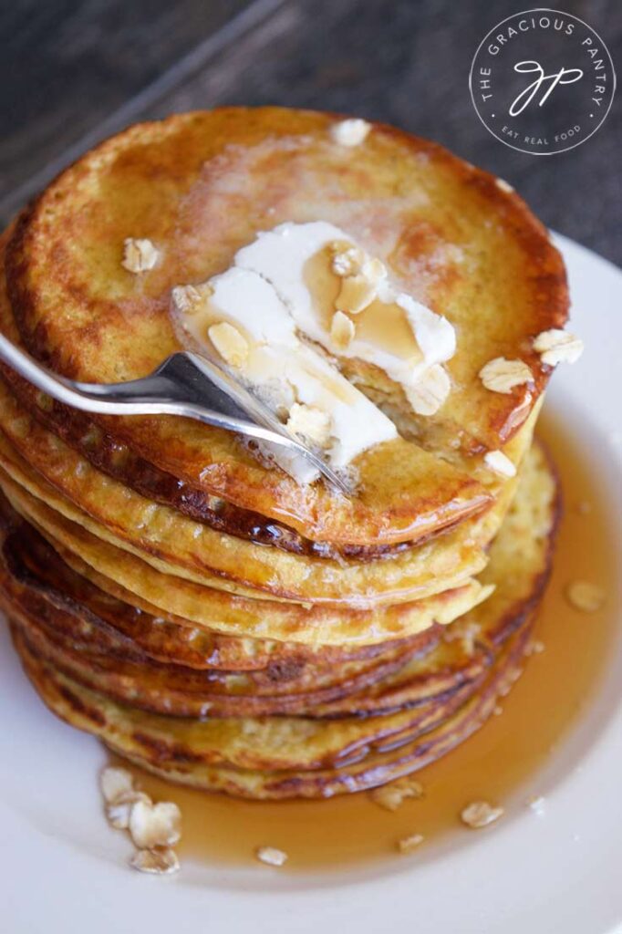 A fork pressing into a warm stack of oat pancakes