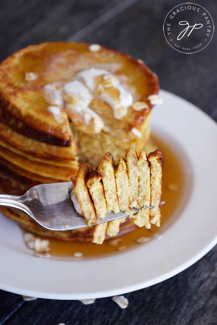 A stack of oat pancakes sits in the background of a fork, holding pancake pieces.