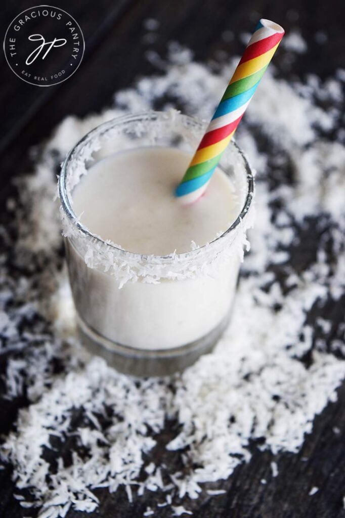 A shot glass filled with this Coconut Milk Smoothie, surrounded by coconut shreds.