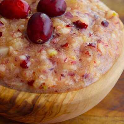 A wooden bowl filled with fresh cranberry relish, topped with three raw cranberries for garnish.