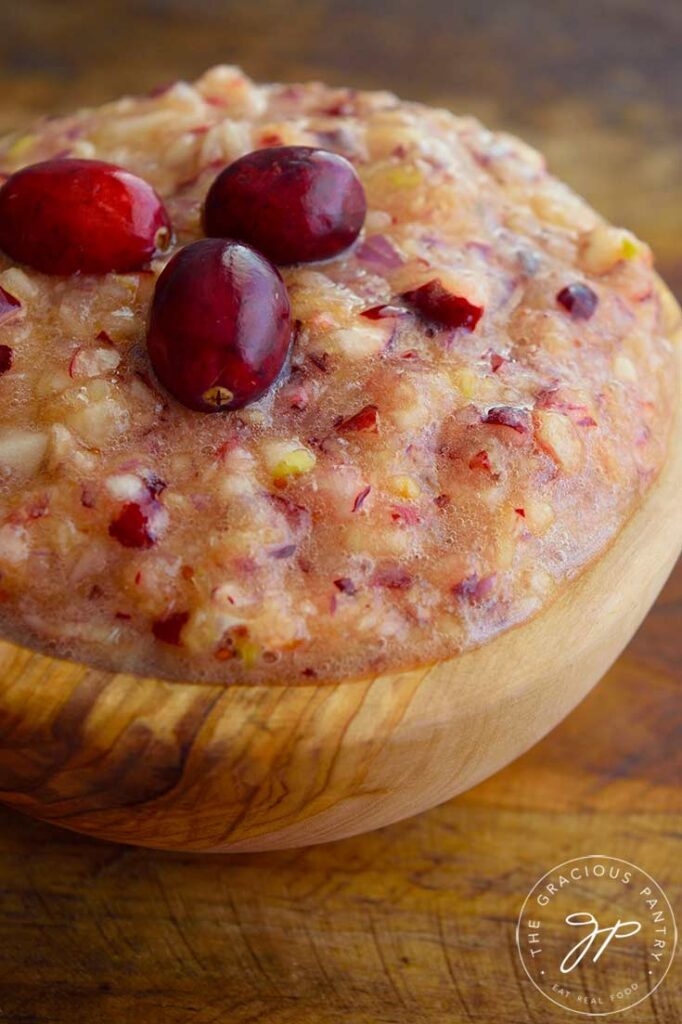 A wooden bowl filled with fresh cranberry relish, topped with three raw cranberries for garnish.