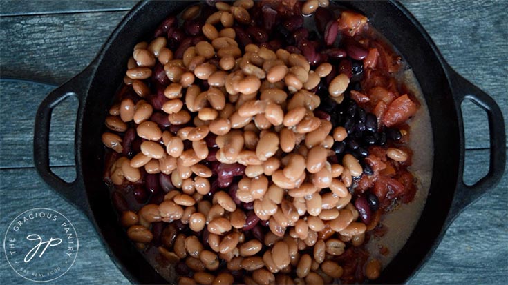 Adding canned pinto beans to the dutch oven for this Dutch Oven Chili Recipe