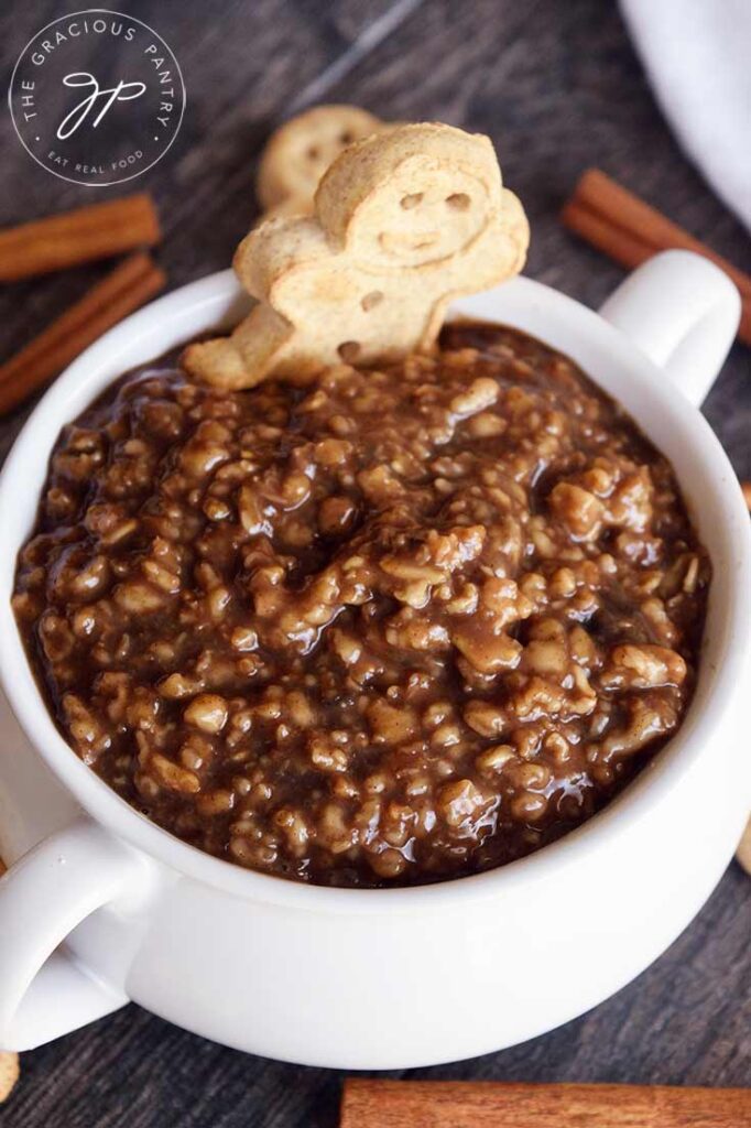 And up close view of this gingerbread oatmeal in a white bowl with a gingerbread man cookie on the edge of the bowl.