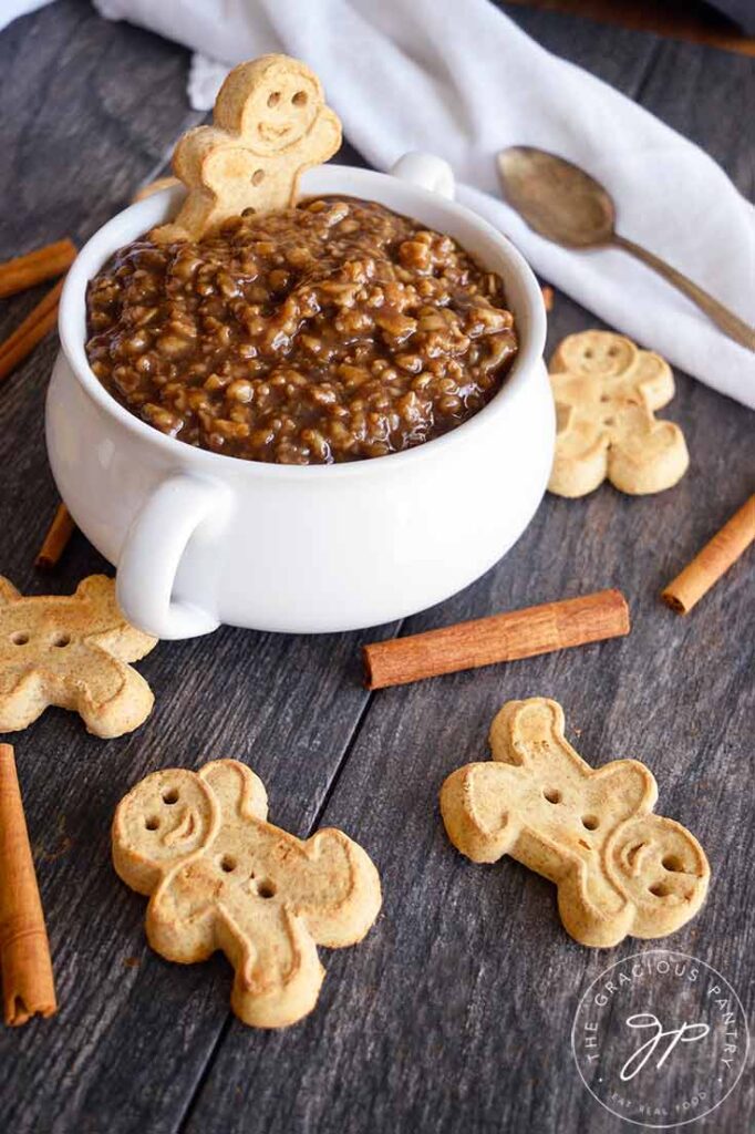 Gingerbread man cookies lay scattered around a while crock filled with gingerbread oatmeal.