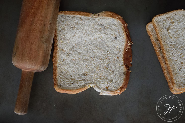 Rolling the slices of bread very flat with a rolling pin.