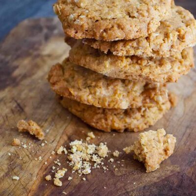 A stack of these Peanut Butter Oatmeal Cookies sit on a cutting board with a few broken pieces sitting in front of the stack.