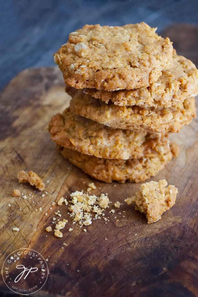 A stack of these Peanut Butter Oatmeal Cookies sit on a cutting board with a few broken pieces sitting in front of the stack.