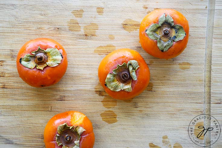 Four whole persimmons sitting on a cutting board about to be made into persimmon pulp.