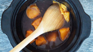 Squishing a persimmon against the side of the slow cooker to check it's doneness.