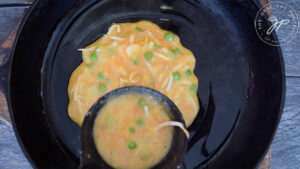 Ladling the egg foo young batter into a skillet to cook.